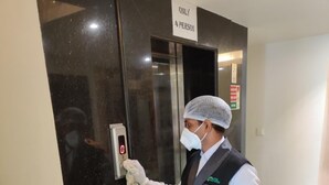 A person in a uniform cleaning a door with a disinfectant spray bottle. - Hotel Shree Vatika (Bhopal)