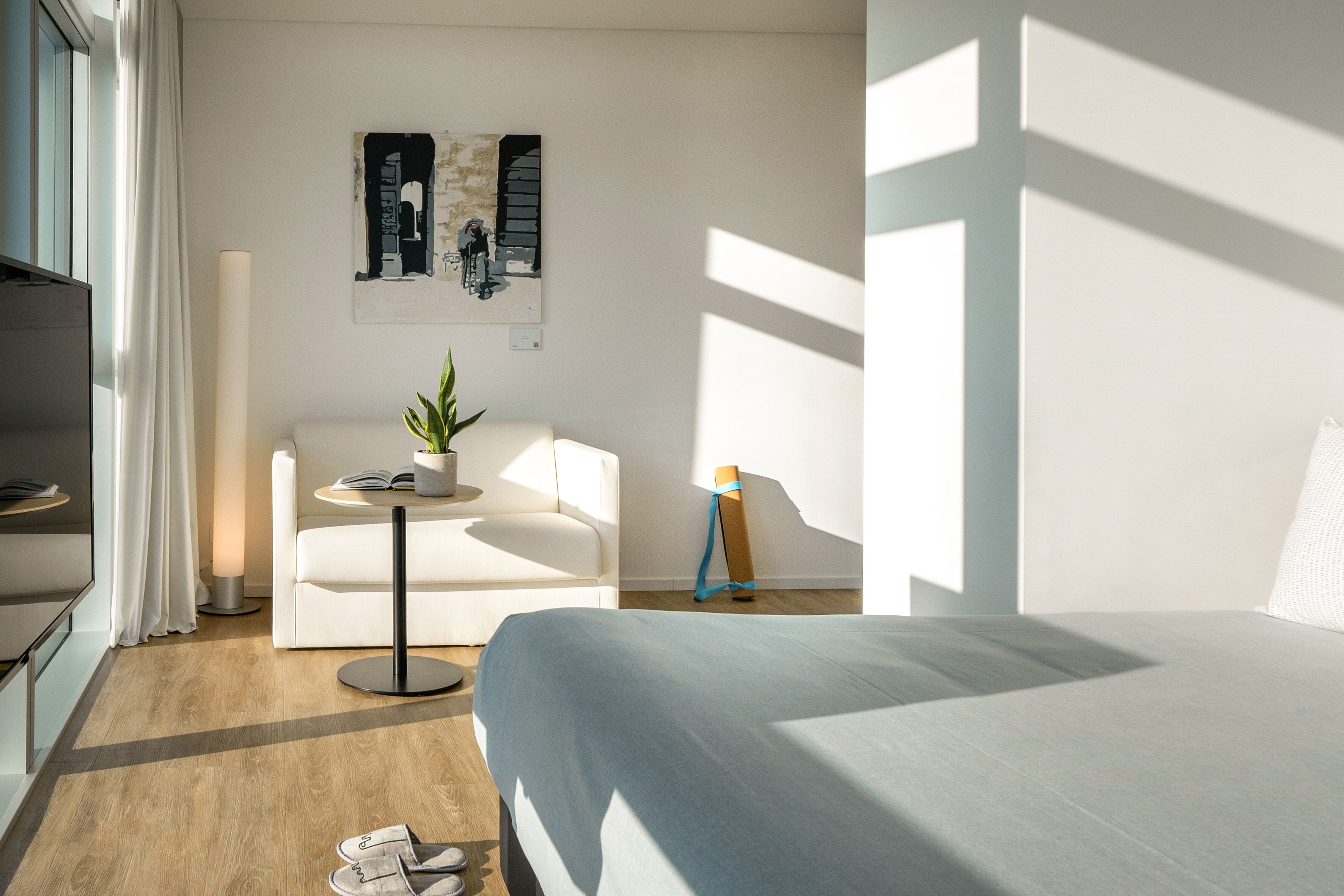 Una habitación de hotel moderna con una cama, un sofá, una mesita con una planta y un cuadro en la pared.