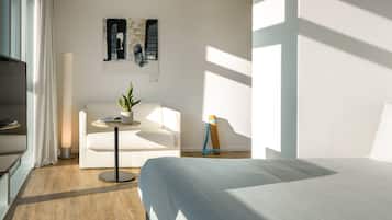 Una habitación de hotel moderna con una cama, un sofá, una mesita con una planta y un cuadro en la pared.