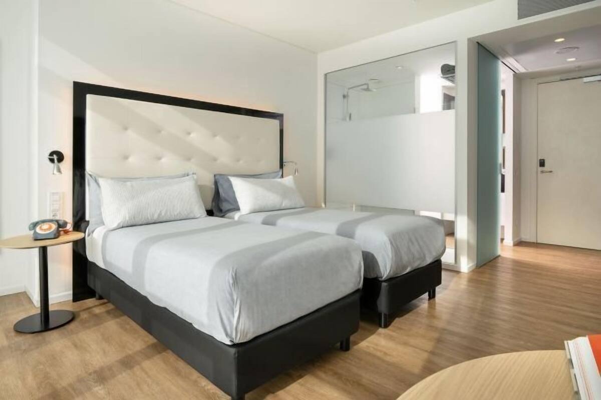 A modern hotel room with a large bed, bedside tables, and a bathroom with a glass shower.