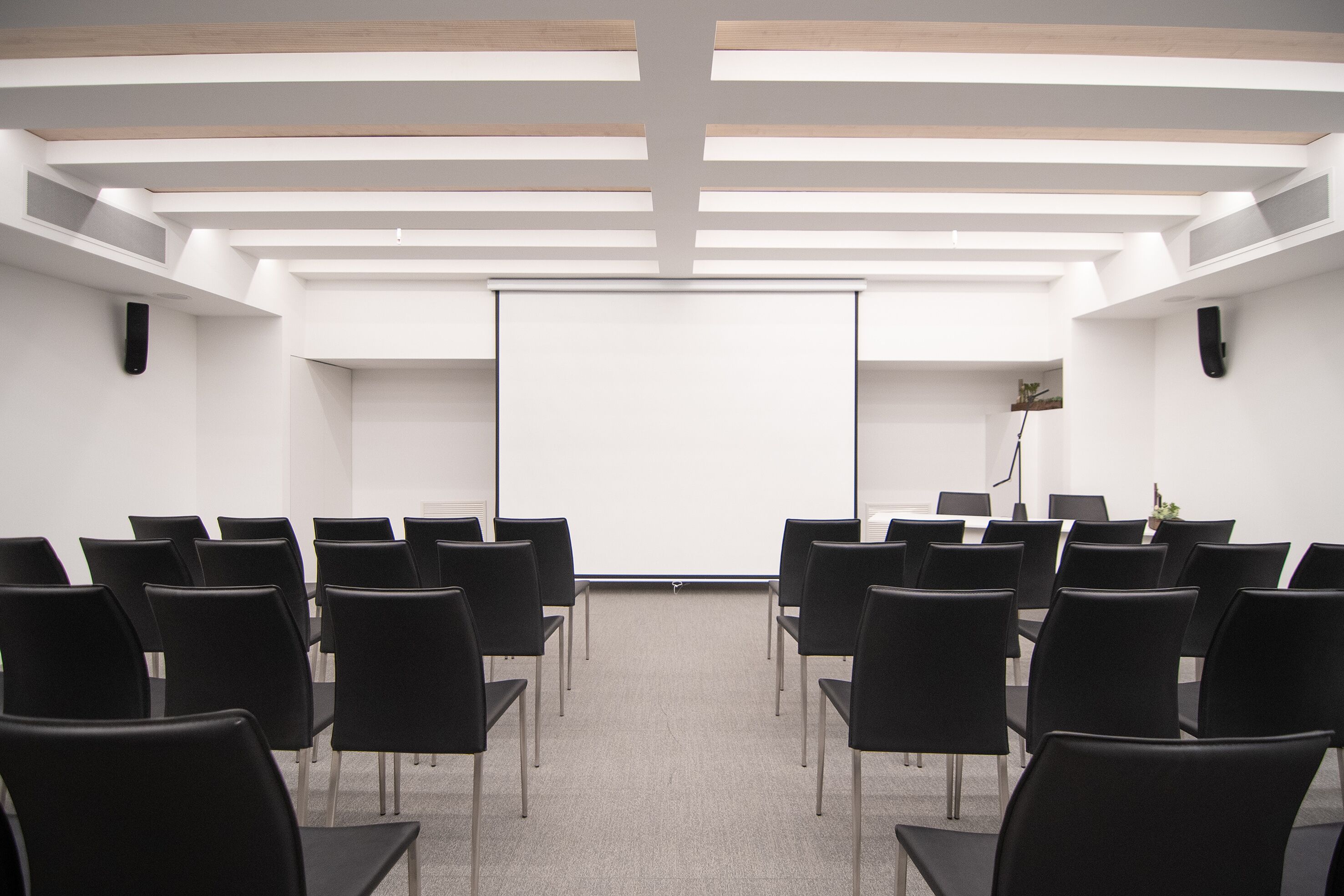 A conference room with rows of black chairs facing a white projection screen.