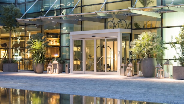 A modern hotel entrance with glass doors, potted plants, and a reflection pool. - INNSiDE by Meliá Milano Torre Galfa (Milan)
