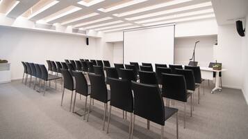 Un salón de conferencias con filas de sillas negras, una pizarra y una pantalla de proyector.