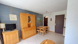 Una habitación con un armario de madera, una mesa de comedor con sillas, un televisor sobre un mueble y una puerta.