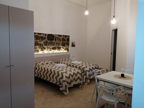 Una habitación pequeña y bien iluminada con dos camas, una pared de piedra, una ventana y un comedor con mesa y sillas.