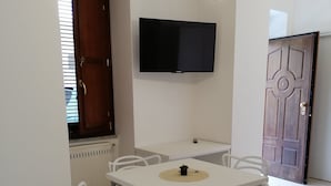 A dining area with a white table and chairs, a mounted TV, and a door with a decorative design. - B&B Ninfa (Caserta)