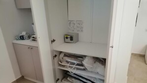 A white cabinet with a microwave on top and a shelf below containing folded blankets and a power strip. - B&B Ninfa (Caserta)