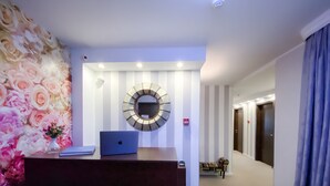 Een hotel receptie met een balie, een laptop, een decoratieve spiegel en een bloemenwand.