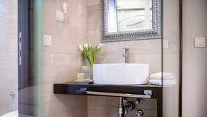 Een moderne badkamer met een douchecabine van glas, een witte wastafel en een spiegel met decoratieve lijst.