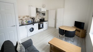 Un espace de vie compact comprenant un coin cuisine, un coin repas avec deux chaises, un canapé et un téléviseur.