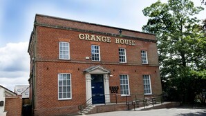 Un bâtiment en briques portant l’inscription « GRANGE HOUSE », avec une entrée centrale, des fenêtres et un petit porche.
