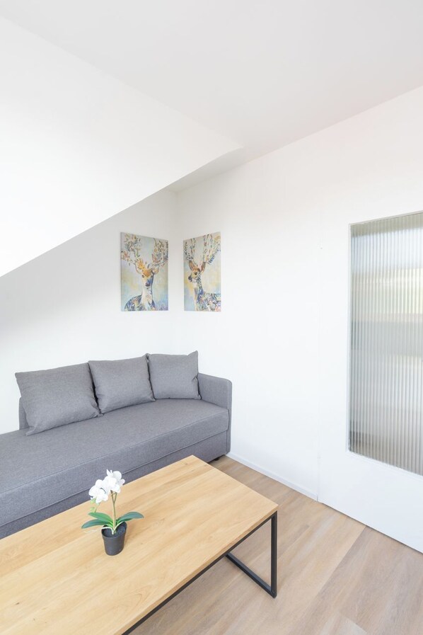 A modern living room with a grey sofa, a wooden coffee table with a potted plant, and two wall-mounted paintings. - Glück Auf Appartements Kammerstraße (Duisburg)