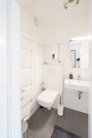 A modern bathroom with a toilet, sink, and mirror. - Glück Auf Appartements Kammerstraße (Duisburg)