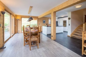 Un'ampia zona pranzo con tavolo e sedie in legno, una cucina sullo sfondo e una scala che conduce a un altro piano.