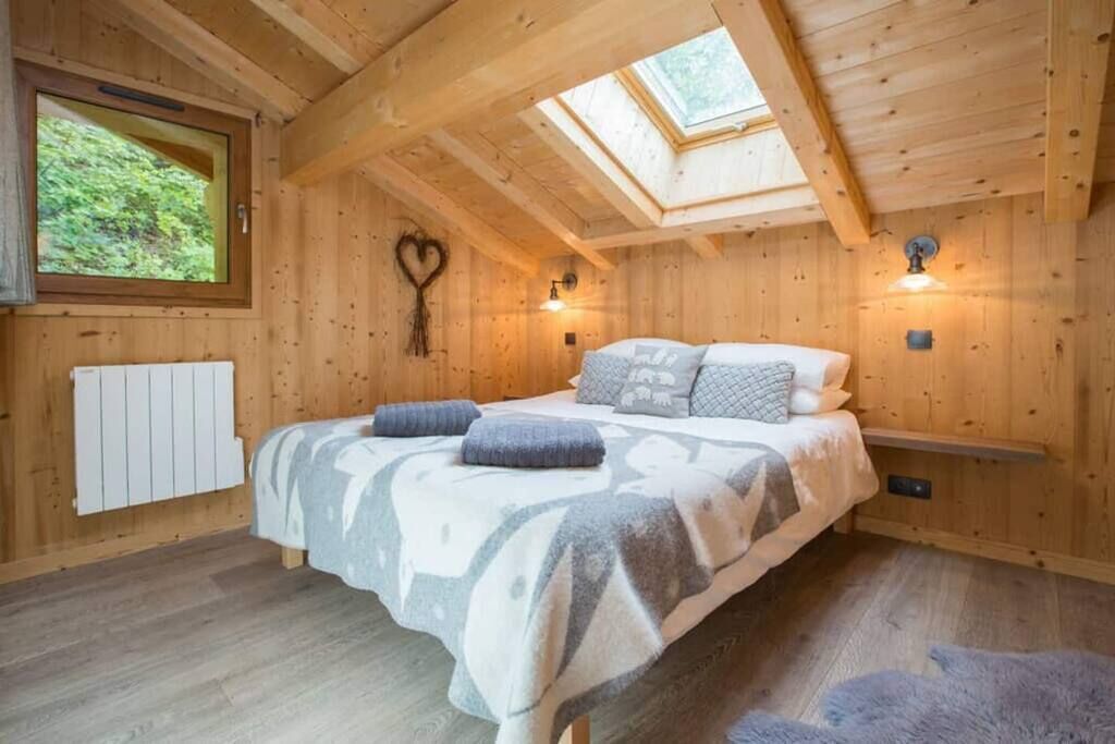 Un dormitorio rústico de cabaña de madera con cama, tragaluz y una decoración con forma de corazón en la pared.