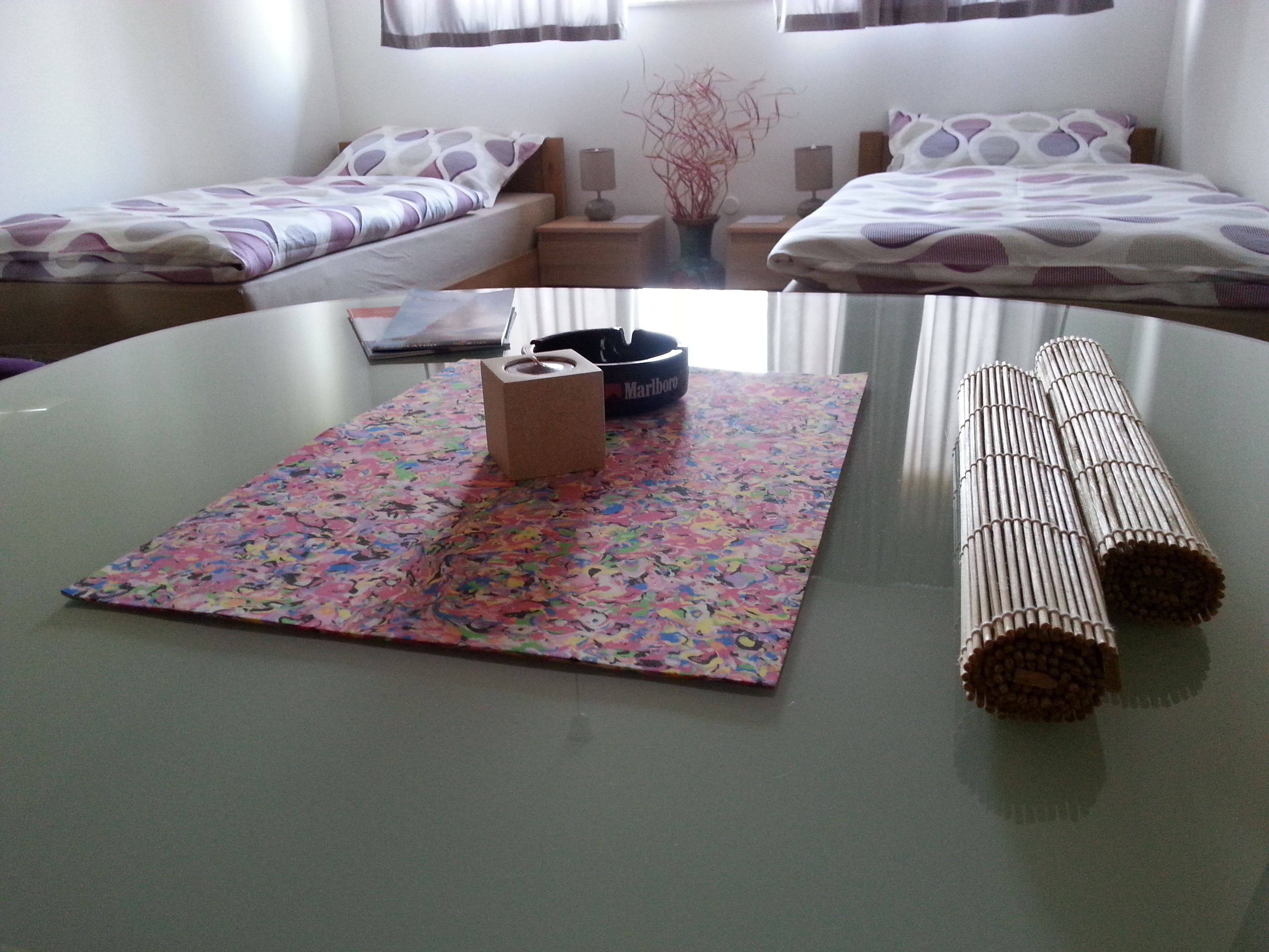 A room with two beds, a table with a colorful mat, a tissue box, and rolled cigarettes.