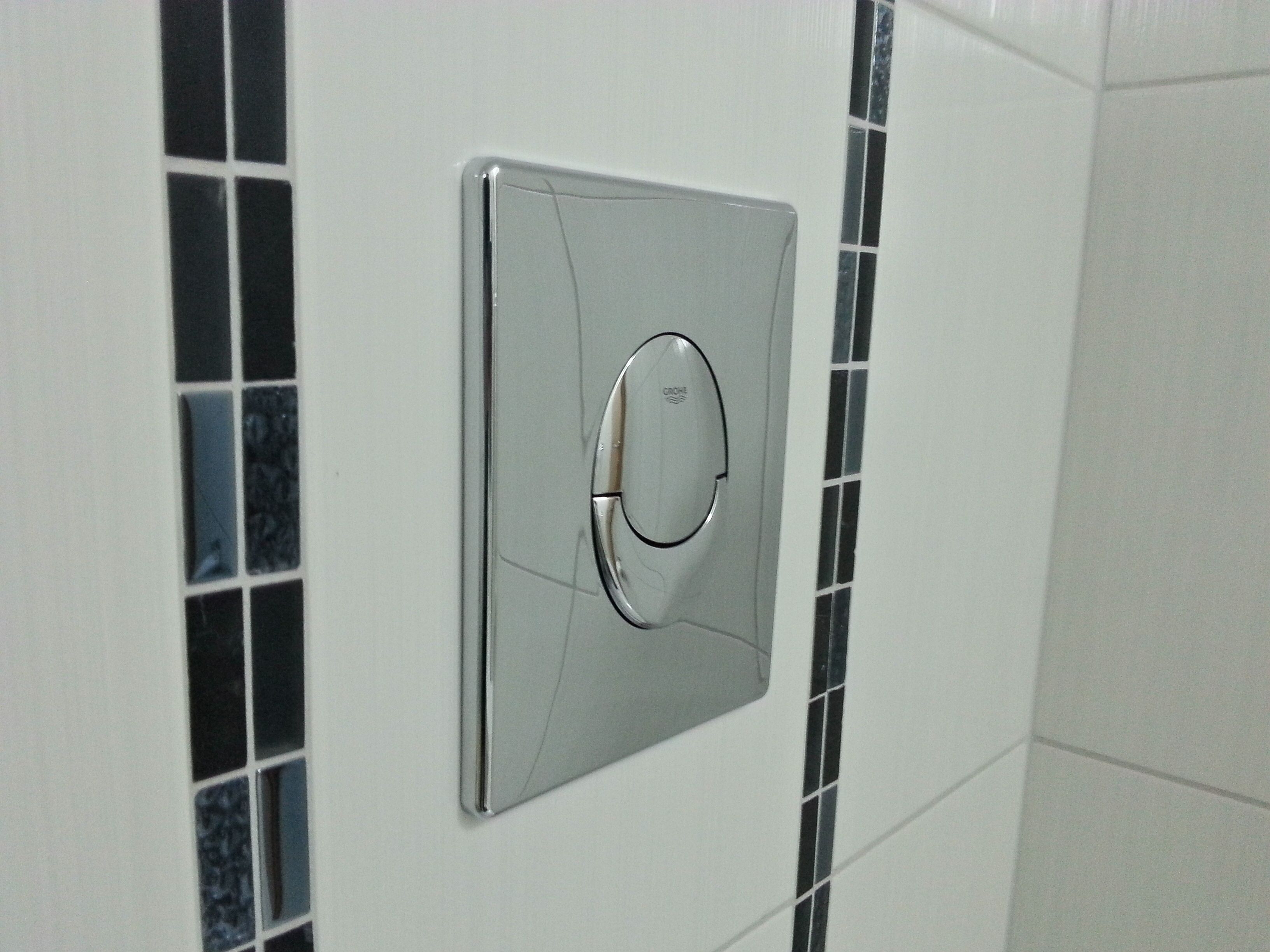 Een aan de muur bevestigde thermostaat met een rond ontwerp, tegen een betegelde muur met een zwart-wit patroon.