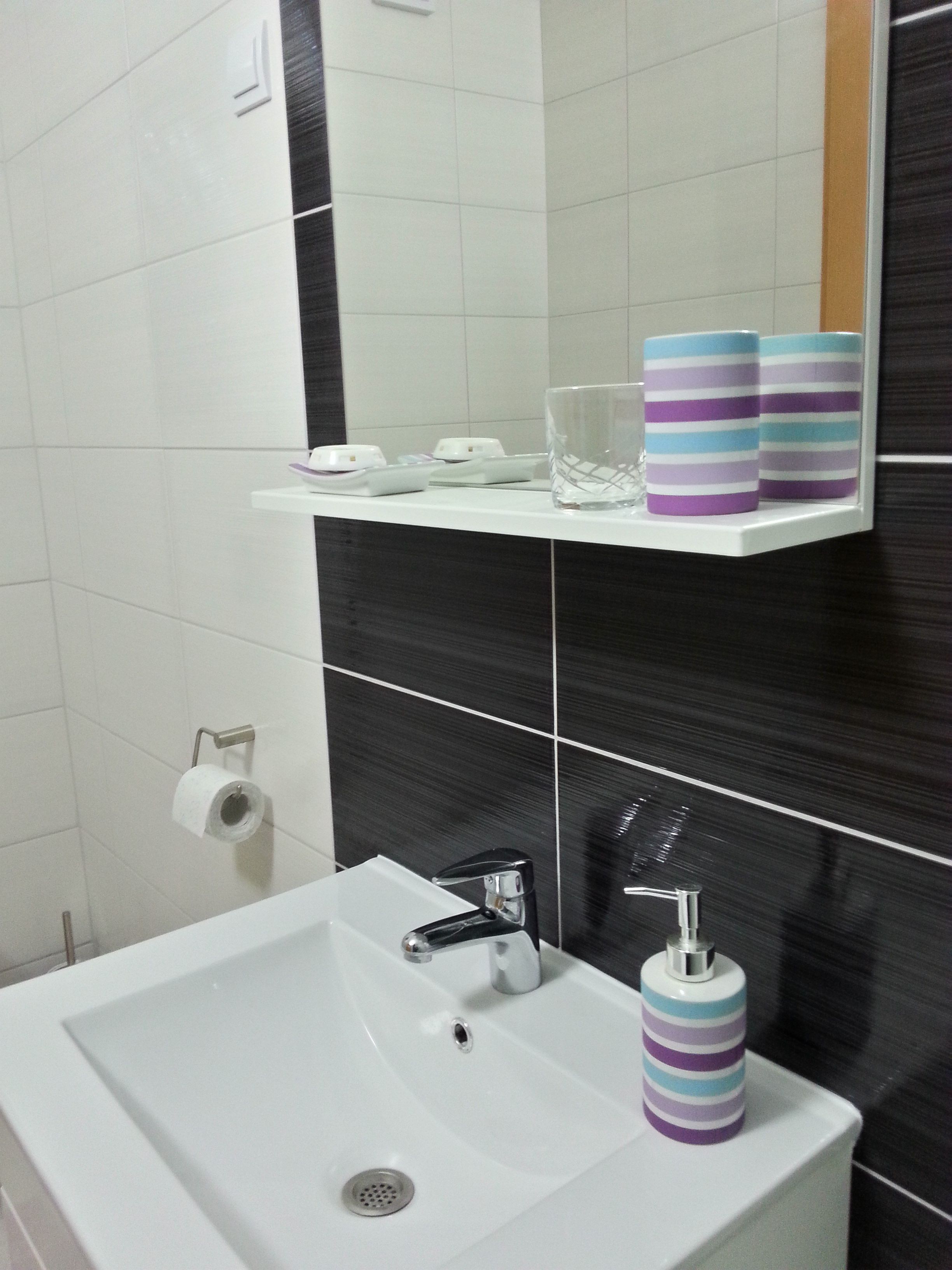 A bathroom with a white sink, a mirror, and a shelf with toiletries.