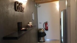 Ein Flur mit Holzboden, einem an der Wand befestigten Schild mit der Aufschrift 'Café', einem Mülleimer und einem Feuerlöscher.