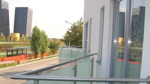 Ein modernes Gebäude mit Glasbalkon und Metallgeländern, mit Blick auf eine Straße mit Bäumen und einem Zaun.
