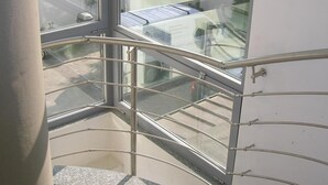 Eine gläserne Treppe mit Metallgeländern, die zu einem Außenbereich mit Blick auf einen Parkplatz und Gebäude führt.