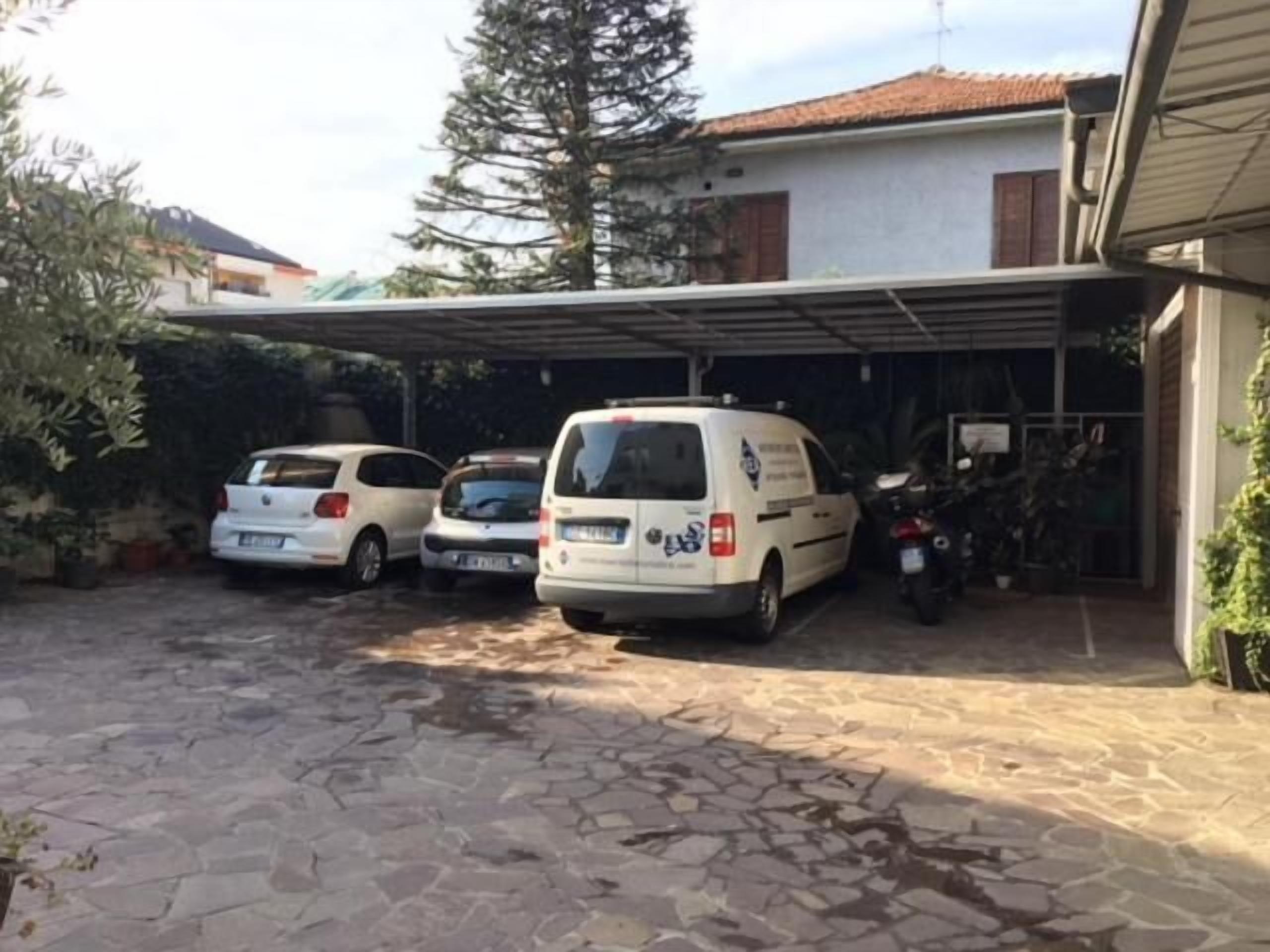 Een overdekte parkeerplaats met drie witte bestelwagens geparkeerd voor een gebouw met een betegeld dak.