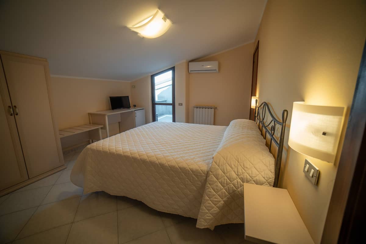 A bedroom with a bed, a desk, a TV, and a window.