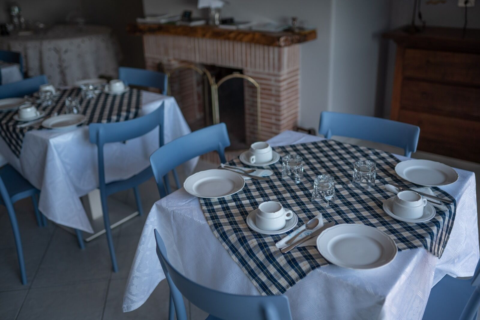 Un comedor con manteles a cuadros, platos blancos y sillas azules.