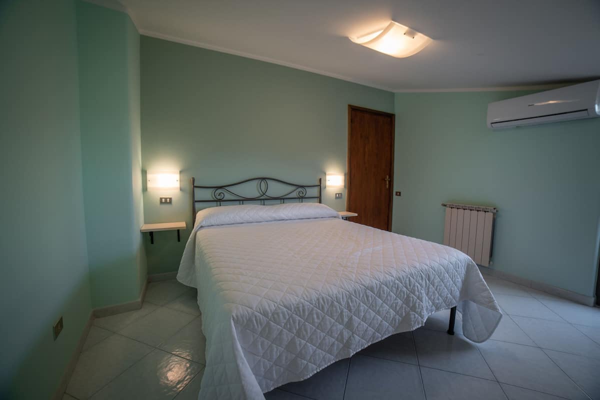 A bedroom with a bed, a nightstand, a wall-mounted air conditioner, and a door.