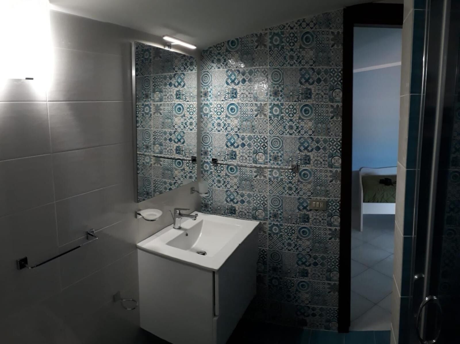 Ein Badezimmer mit einem weißen Waschbecken, einem Spiegel und Wandfliesen mit Muster.