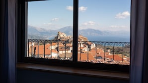 A view from a window overlooking a town with red-roofed buildings and mountains in the background.