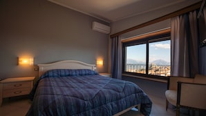 A bedroom with a large bed, bedside tables, an air conditioning unit, a chair, and a window with a view of mountains.