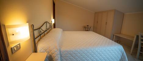 A bedroom with a bed, bedside table, lamp, wardrobe, and a small table.