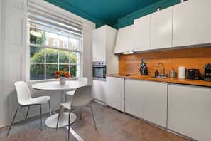 Una cocina moderna con armarios blancos, encimera de madera y ventana con vistas a la vegetación.