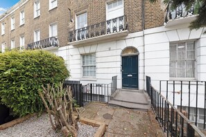 Une maison de ville avec une porte d’entrée bleu foncé, une façade en briques blanches et un petit jardin à l’avant.