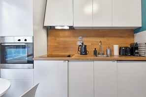Een moderne keuken met witte kastjes, een houten aanrecht, een inbouwoven, een koffiezetapparaat en een broodrooster.