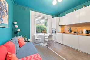Un espacio habitable compacto con kitchenette, comedor y sofá con cojines.
