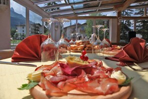 Mesa servida con comida y copas de vino, con vista a montañas y edificios al fondo.