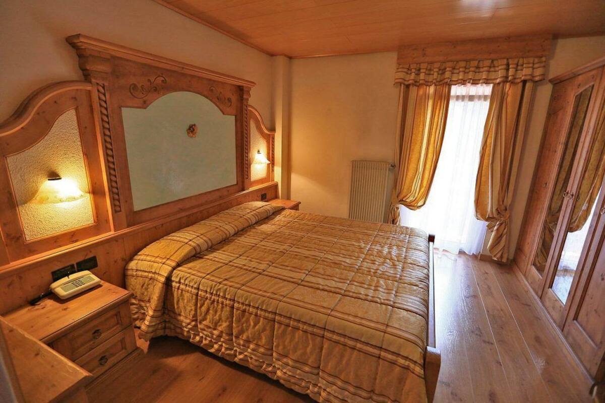 Ein Schlafzimmer mit Holzbettrahmen, einem Nachttisch, einer Lampe und Vorhängen.