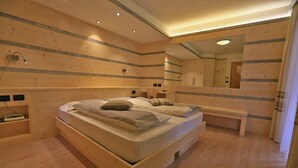 Een slaapkamer met een houten bed, nachtkastje, spiegel en een bankje.