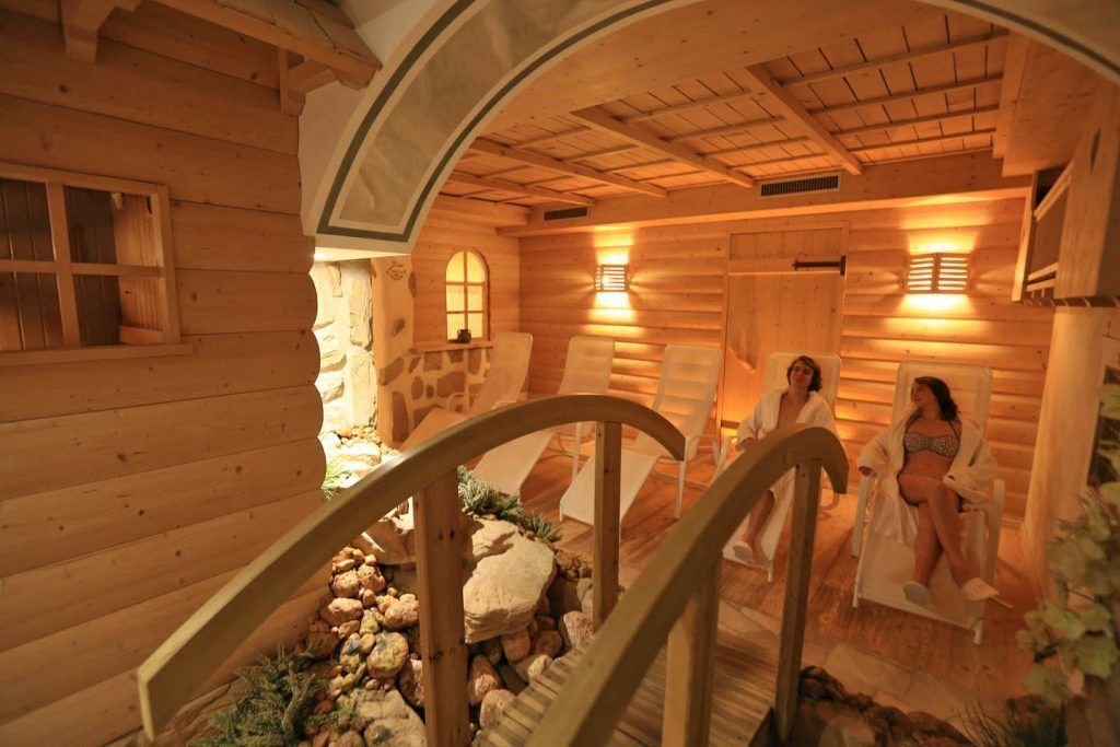 A wooden cabin interior with a stone wall, wooden benches, and a wooden staircase.