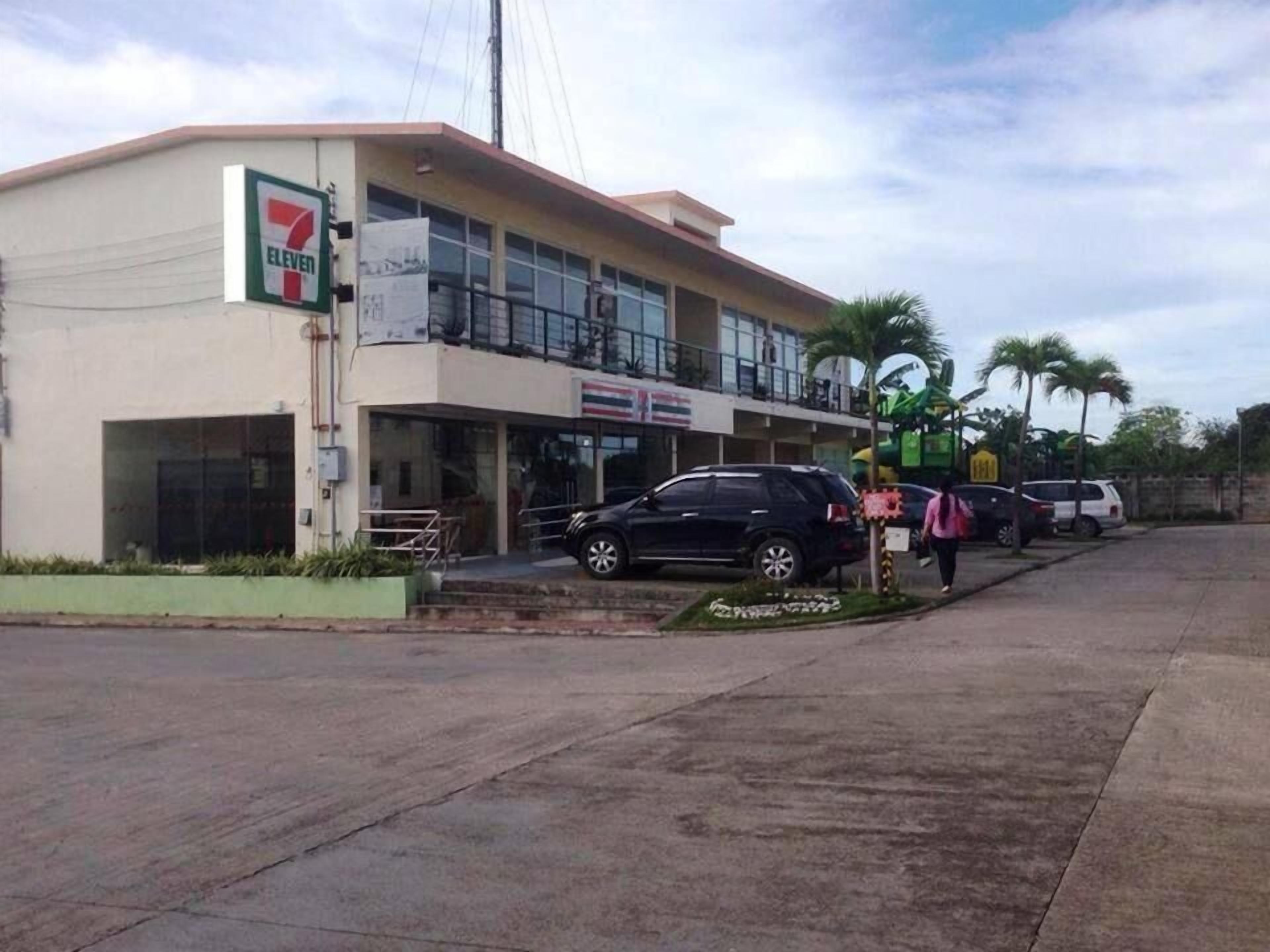 A 7-Eleven convenience store with a two-story building, a covered entrance, and a parking area with several cars.