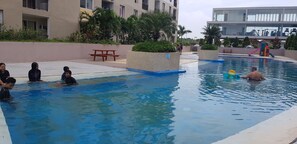 A swimming pool with people in the water, surrounded by buildings and greenery.