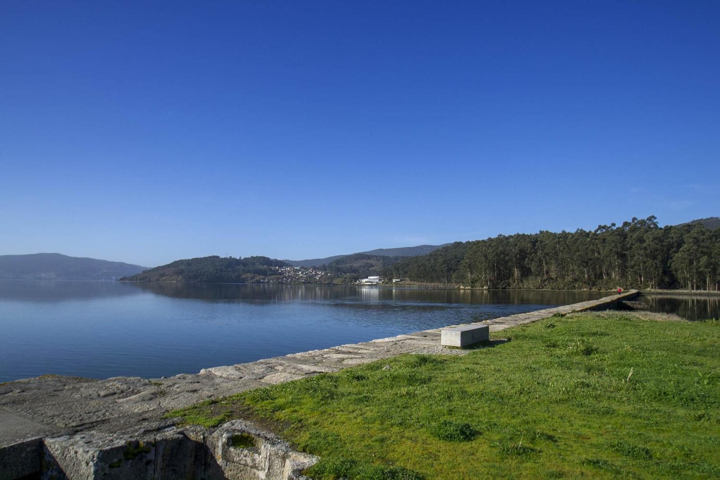 Un lago tranquilo con un muro de hormigón y un edificio pequeño en la orilla opuesta.