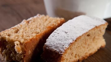 Una fetta di torta con zucchero a velo e una tazza di caffè su un tavolo di legno.