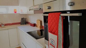 Une cuisine moderne avec des armoires blanches, un four en acier inoxydable et un manique rouge accroché à la poignée du four.