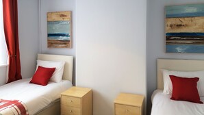 Une chambre avec deux lits, chacun agrémenté de draps blancs et d’oreillers rouges, une suspension rouge et deux tableaux accrochés aux murs.
