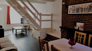 Un intérieur moderne avec un escalier, un coin repas comprenant une table et des chaises, et un mur en briques orné de tableaux encadrés.