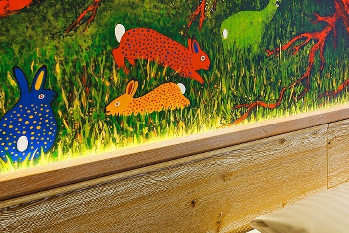 Habitación de hotel con cama, cortina a rayas de colores, un mural en la pared y una lámpara de noche.