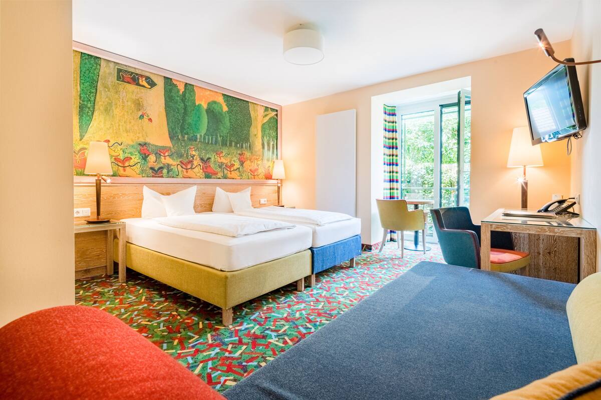 Habitación de hotel con cama, escritorio, silla, televisor y un amplio ventanal.